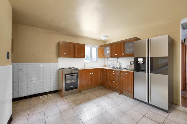 kitchen with sink, appliances with stainless steel finishes, light tile patterned floors, and tile walls