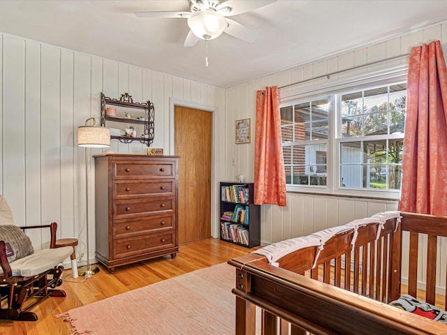 bedroom featuring wooden walls, a nursery area, hardwood / wood-style flooring, and ceiling fan