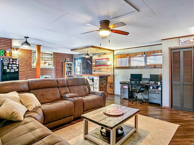 living room with wood walls, hardwood / wood-style flooring, ceiling fan, and brick wall