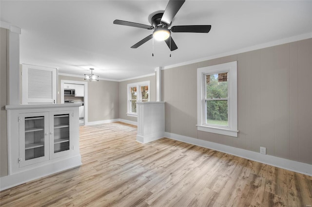 unfurnished living room with ceiling fan with notable chandelier, light hardwood / wood-style floors, ornamental molding, and wood walls