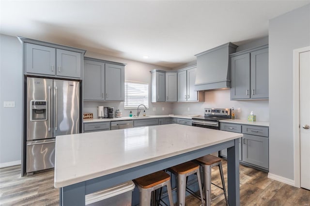 kitchen with premium range hood, sink, stainless steel appliances, dark hardwood / wood-style floors, and a kitchen breakfast bar