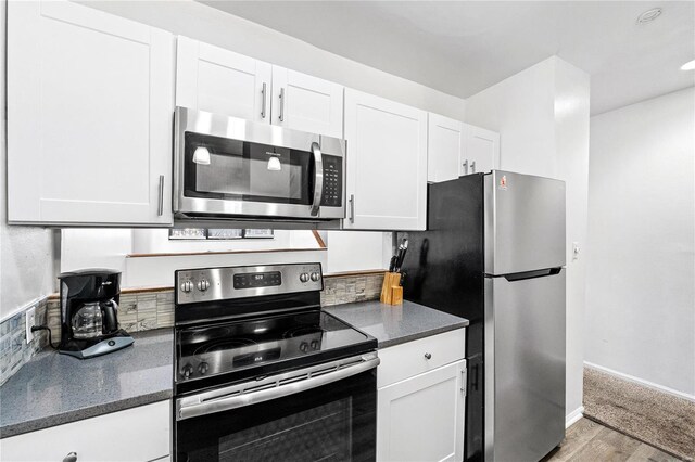 kitchen featuring white cabinets, appliances with stainless steel finishes, light wood-type flooring, and dark stone counters