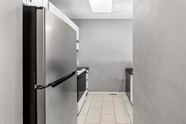 kitchen with stainless steel refrigerator, light tile patterned flooring, electric range, and white cabinetry