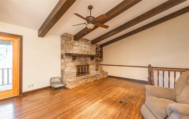 unfurnished living room featuring ceiling fan, a stone fireplace, wood-type flooring, and lofted ceiling with beams