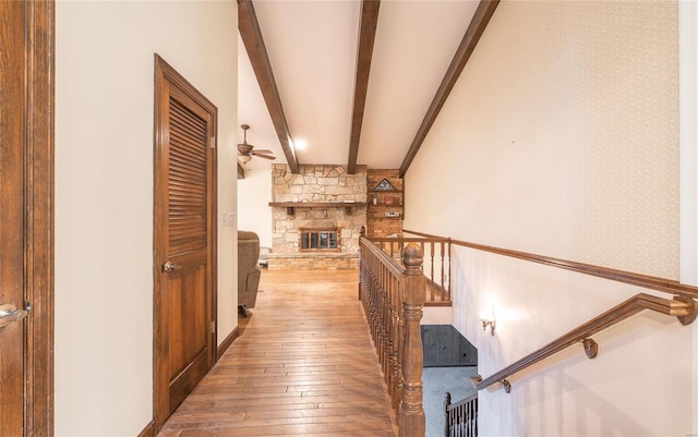 hallway featuring beamed ceiling, wood-type flooring, an upstairs landing, and wallpapered walls