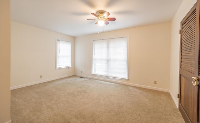 spare room with a ceiling fan, light colored carpet, visible vents, and baseboards