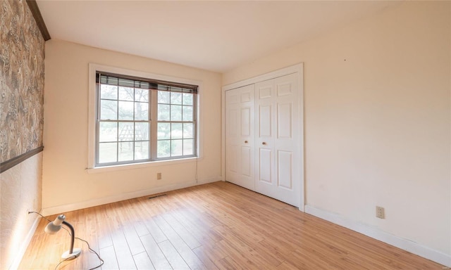 unfurnished bedroom featuring a closet, visible vents, baseboards, and wood finished floors