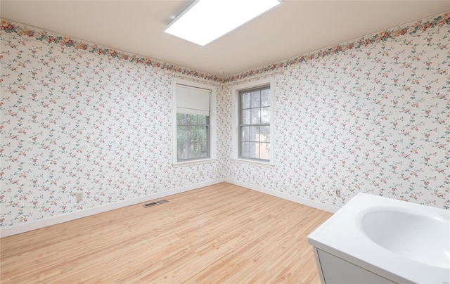 empty room with wallpapered walls, baseboards, visible vents, and light wood finished floors