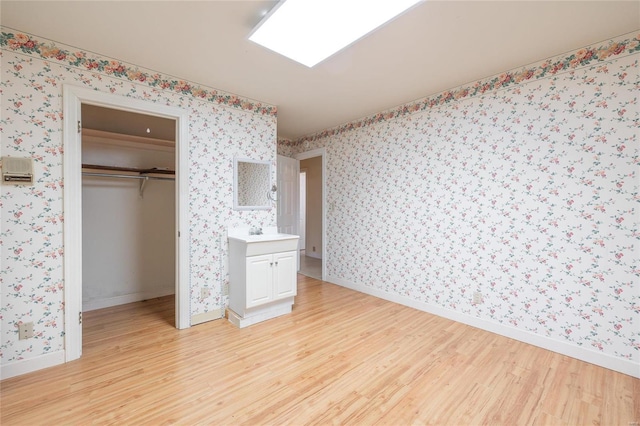 unfurnished bedroom with baseboards, light wood-style floors, a closet, and wallpapered walls