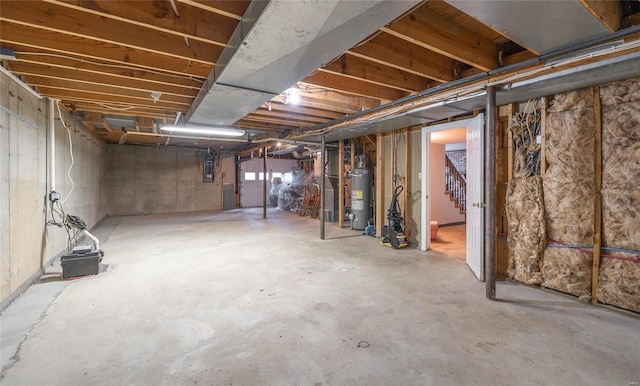 basement featuring electric panel, water heater, and stairway