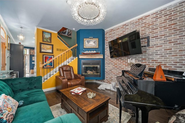 living room featuring wood-type flooring, an inviting chandelier, ornamental molding, and brick wall