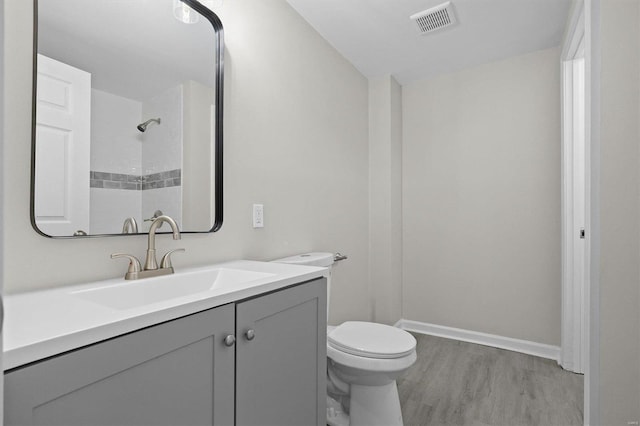 bathroom with tiled shower, vanity, toilet, and wood-type flooring