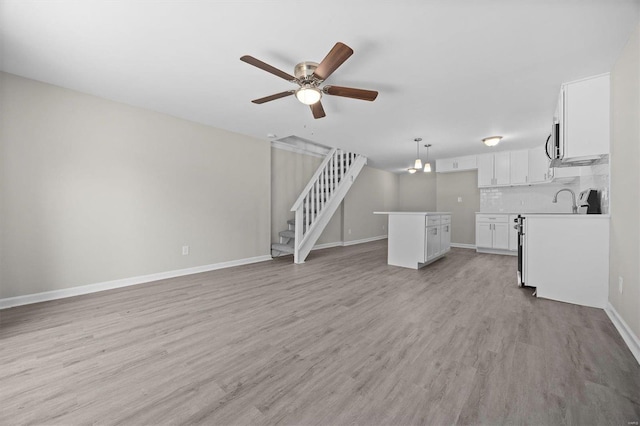 unfurnished living room featuring ceiling fan with notable chandelier and light hardwood / wood-style flooring