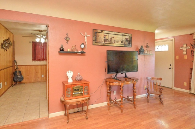 living room featuring ceiling fan, light wood-type flooring, and wooden walls