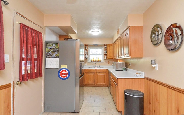 kitchen featuring sink, light tile patterned flooring, wooden walls, and stainless steel fridge