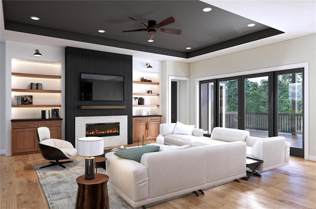 living room featuring a fireplace, light wood-type flooring, a tray ceiling, and ceiling fan