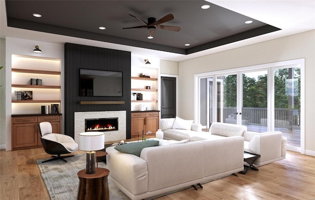 living room with light hardwood / wood-style flooring, ceiling fan, a fireplace, built in shelves, and a raised ceiling