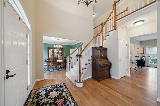 entryway featuring a towering ceiling, ornamental molding, light hardwood / wood-style floors, and a chandelier