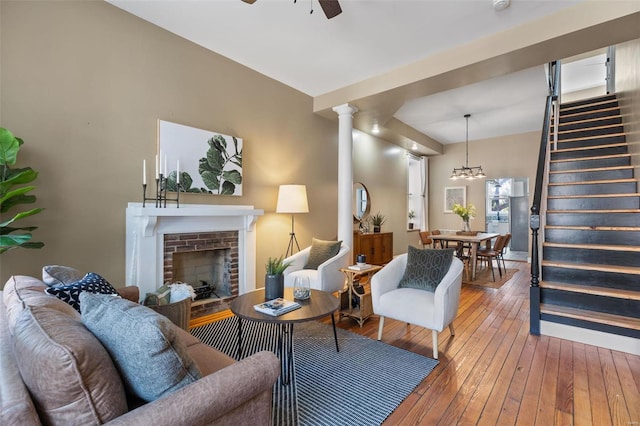 living room featuring ornate columns, ceiling fan with notable chandelier, hardwood / wood-style flooring, and a fireplace