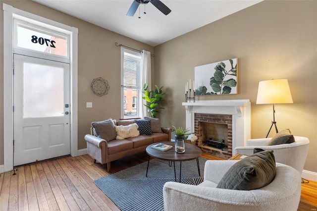 living room with ceiling fan, hardwood / wood-style floors, and a brick fireplace