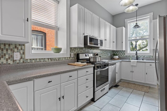 kitchen featuring decorative light fixtures, stainless steel appliances, light tile patterned floors, sink, and white cabinets