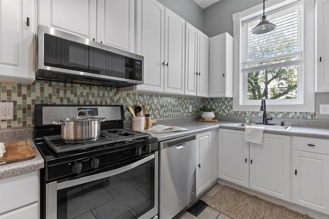 kitchen with pendant lighting, white cabinets, sink, appliances with stainless steel finishes, and light tile patterned flooring