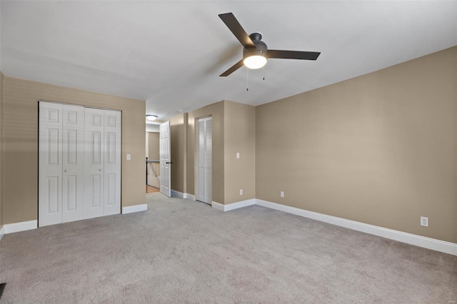 unfurnished bedroom with ceiling fan, light carpet, and multiple closets