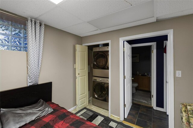 bedroom featuring stacked washer / dryer, a drop ceiling, and dark tile patterned flooring