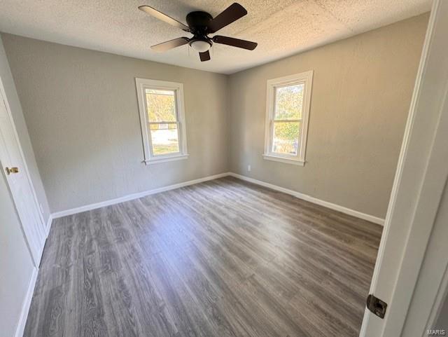 empty room with ceiling fan, plenty of natural light, dark wood-type flooring, and a textured ceiling