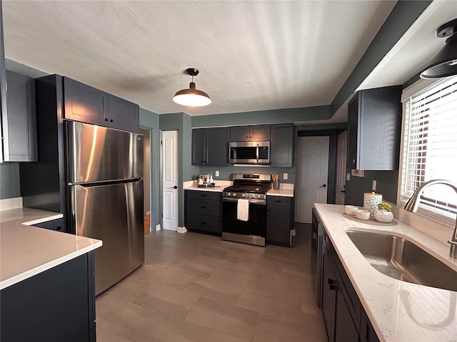 kitchen featuring light stone countertops, sink, pendant lighting, a textured ceiling, and appliances with stainless steel finishes