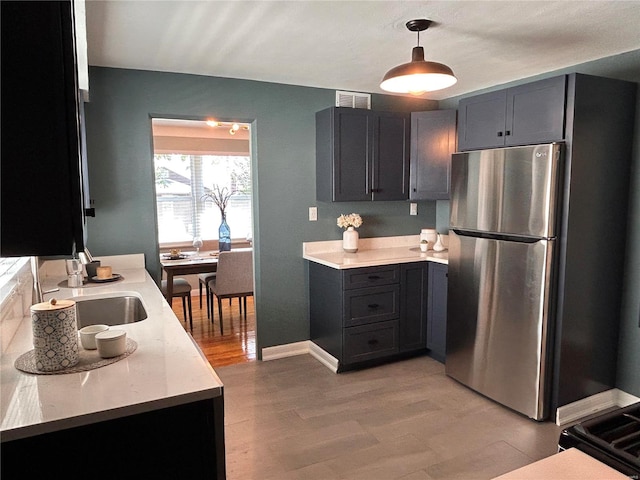 kitchen with decorative light fixtures, light hardwood / wood-style floors, sink, and stainless steel refrigerator