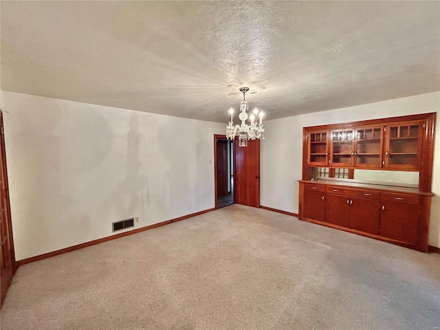 unfurnished room with light carpet, a textured ceiling, and a notable chandelier