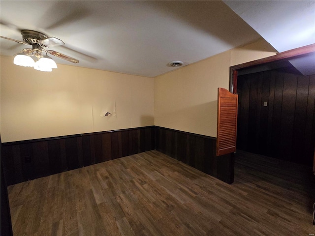 unfurnished room featuring dark hardwood / wood-style flooring, wooden walls, and ceiling fan