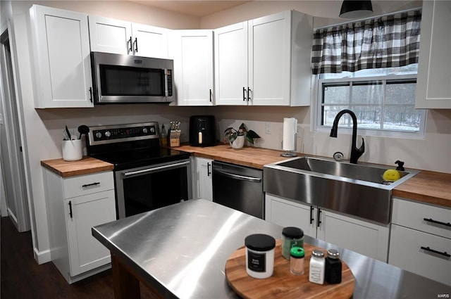 kitchen featuring wood counters, stainless steel appliances, white cabinetry, sink, and dark wood-type flooring