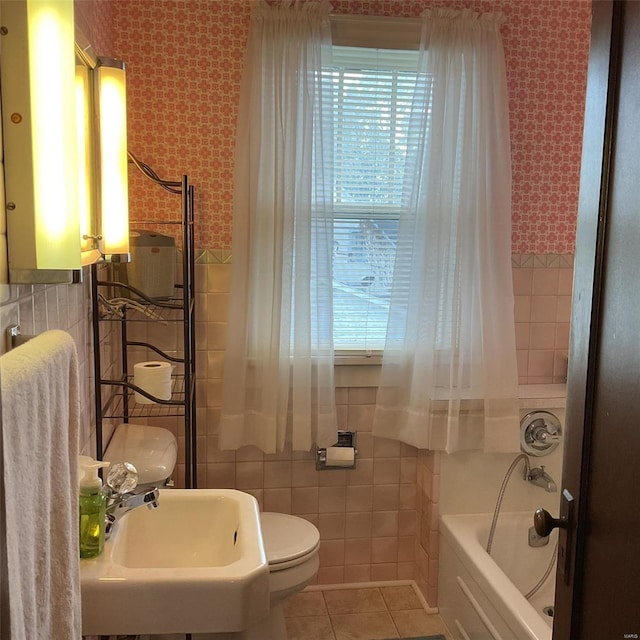 bathroom with toilet, a bathtub, tile patterned flooring, and tile walls