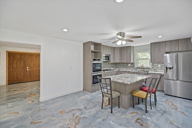 kitchen featuring appliances with stainless steel finishes, a center island, ceiling fan, and tasteful backsplash