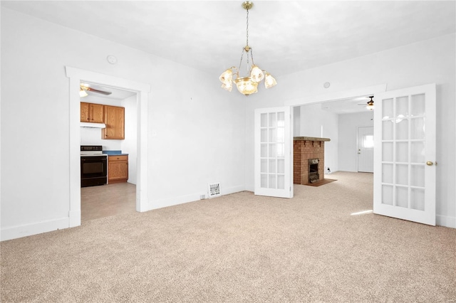 unfurnished living room featuring a fireplace, ceiling fan with notable chandelier, light colored carpet, and french doors