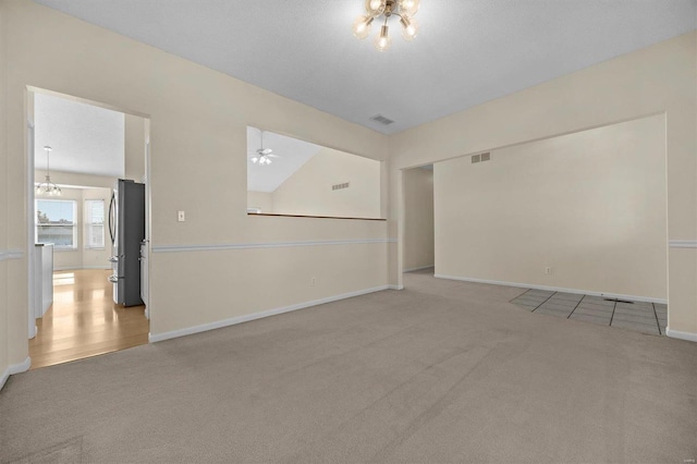 carpeted spare room featuring a textured ceiling, ceiling fan with notable chandelier, and vaulted ceiling