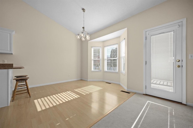 unfurnished dining area featuring light hardwood / wood-style floors, a textured ceiling, and a chandelier