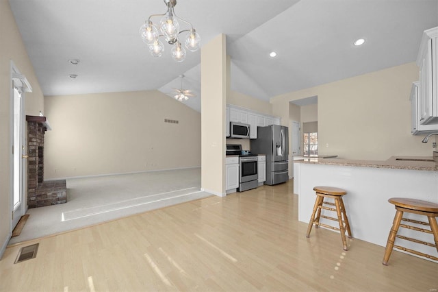 kitchen with white cabinetry, sink, stainless steel appliances, vaulted ceiling, and a kitchen bar