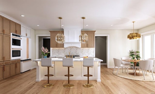 kitchen with hanging light fixtures, an island with sink, high end white refrigerator, light hardwood / wood-style flooring, and a chandelier