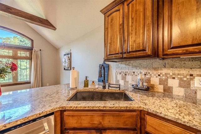 kitchen featuring light stone countertops, stainless steel dishwasher, vaulted ceiling, and sink