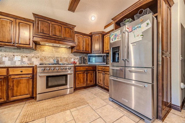 kitchen with light tile patterned flooring, high quality appliances, custom range hood, and decorative backsplash