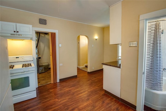 kitchen featuring dark hardwood / wood-style flooring, gas range gas stove, dark stone countertops, and white cabinets