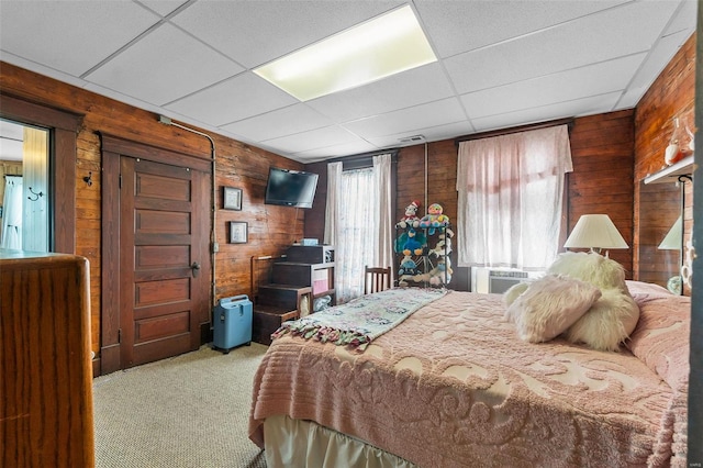 bedroom featuring a drop ceiling, wooden walls, and light carpet