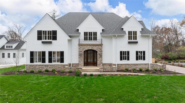 view of front of house with a balcony, stone siding, a front lawn, and roof with shingles