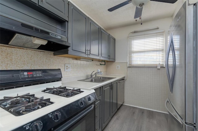 kitchen featuring sink, hardwood / wood-style flooring, appliances with stainless steel finishes, gray cabinetry, and ventilation hood