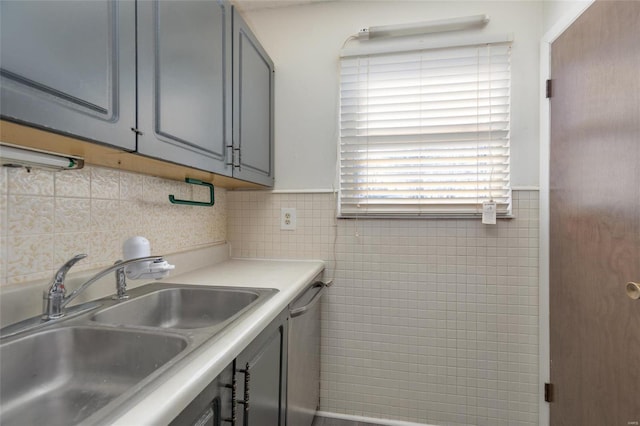 kitchen with stainless steel dishwasher, sink, tile walls, and gray cabinetry