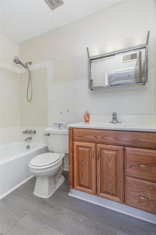 full bathroom featuring tiled shower / bath combo, vanity, tile walls, and toilet