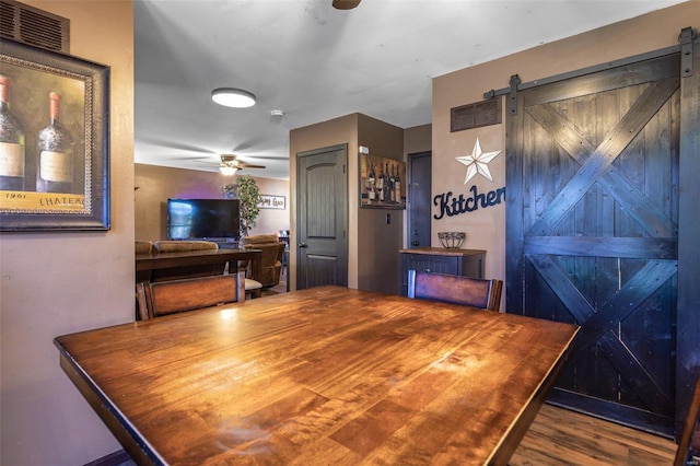 dining room with wood-type flooring, a barn door, and ceiling fan